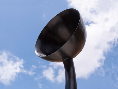 A bronze bowl-like head jutting into the sky with a bright blue sky and clouds in the background