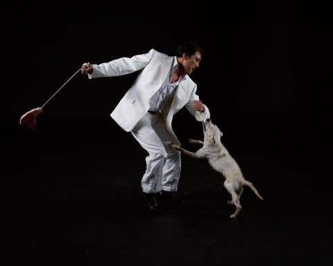 A man swinging a raw steak on a rope while a dog bites his sleeve