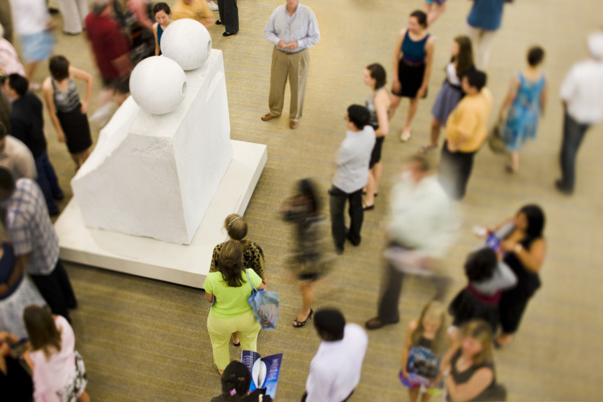 A crowd of people around a large rectangular marble sculpture with spheres on top