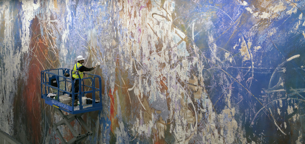 A man on scissor lift paints a mural. 