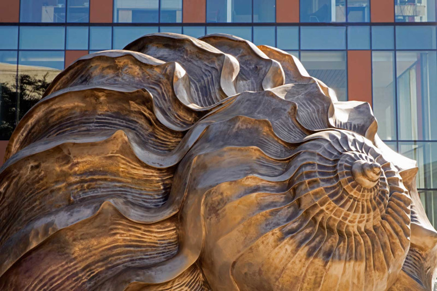 The spiral of the large bronze shell with a building behind it