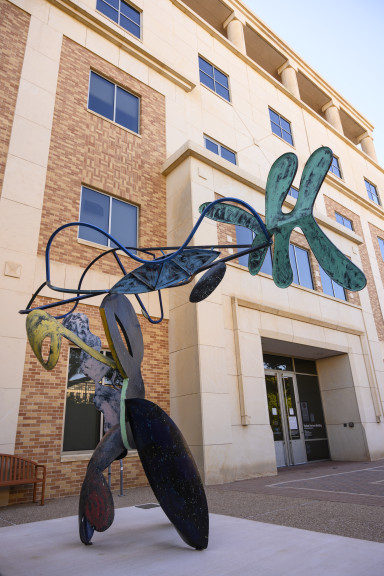 A large bendy sculpture with parts colored in different colors in front of a brick building with windows