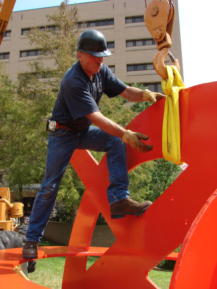 A man working on a large red metal sculpture