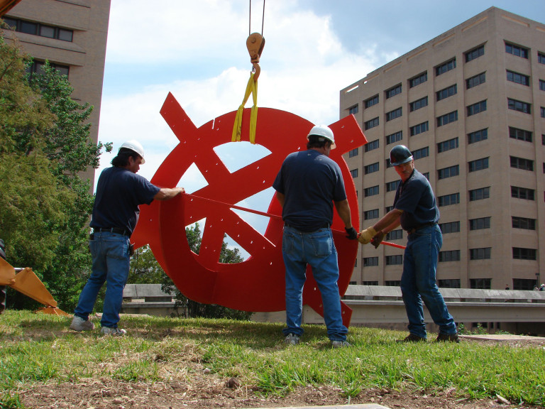 Men working on a large red metal sculpture