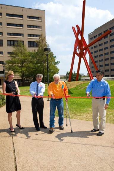 Four people cutting a ribbon in front of a large metal sculpture