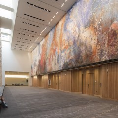 person sitting on bench in big atrium with mural on the opposite wall