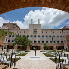 Sentinel IV, seen from behind. The work is centered in a landscaped courtyard. An apeture created by the building frames the work in this image with the circular ceiling coming down and two staircases framing the bottom edge.
