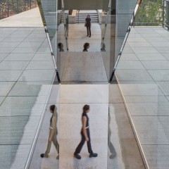 A detail of Sarah Oppenheimer's "C-010106," which shows the reflective quality of the work under the bridge. Multiple figures are caught in the visual reflection of the inside.