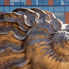 The spiral of the large bronze shell with a building behind it