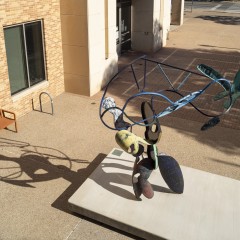 A large bendy sculpture with parts colored in different colors in a courtyard as seen from above