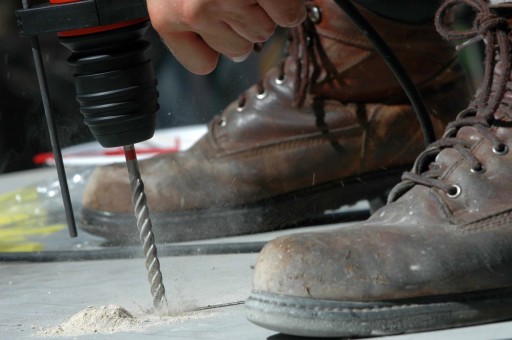 A close up of a drill drilling into concrete while dust pours out. 