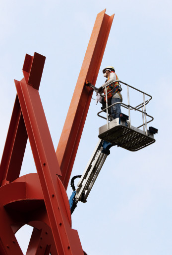 A worker in a cherrypicker sands the red surface of Mark di Suvero's "Clock Knot"
