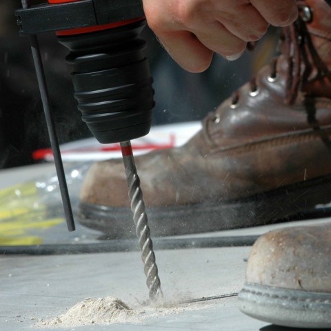 A close up of a drill drilling into concrete while dust pours out. 