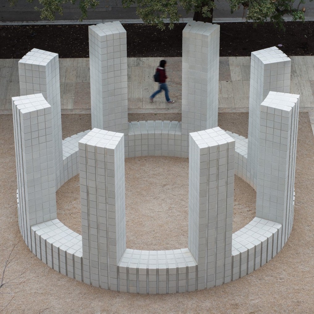 A circular structure of white concrete brick with 8 pillars seen from above