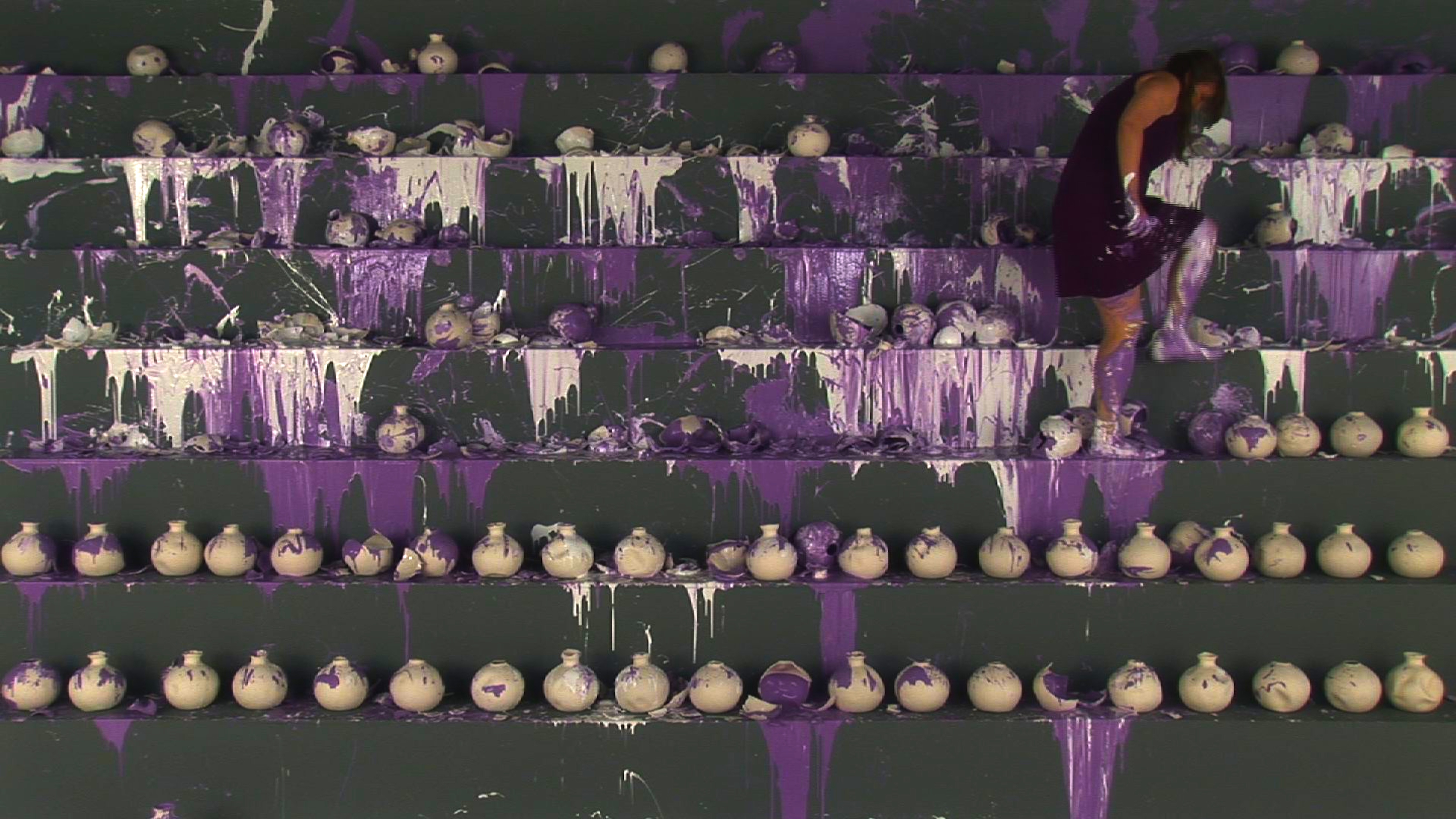 Artist stomping and breaking clay jars of white and purple paint