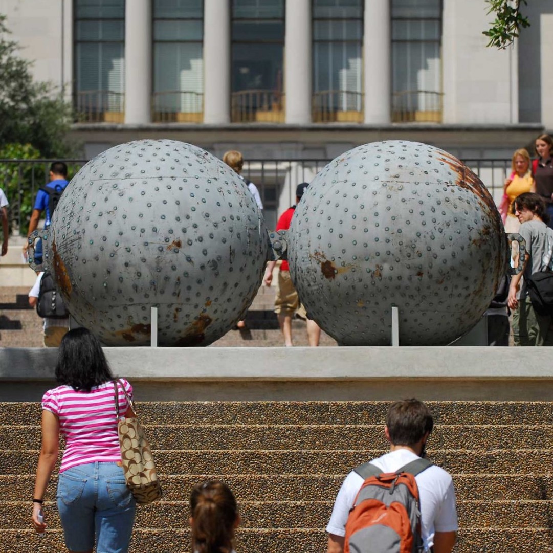 Two large buoys covered in pennies are set atop a number of stairs with people walking up and around them 