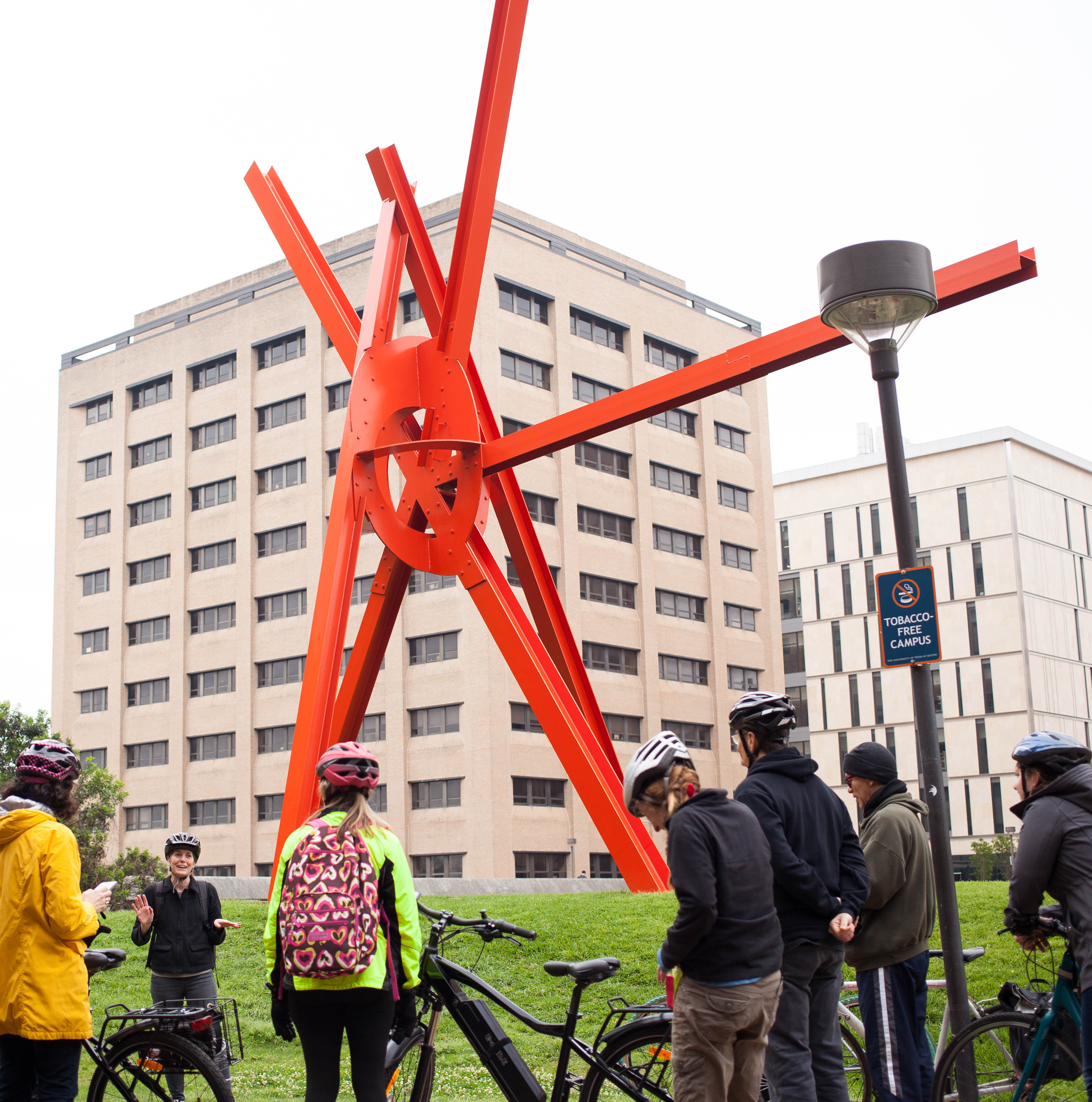 A group of people with bikes wear helmets and stand looking at Marc di Suvero's 