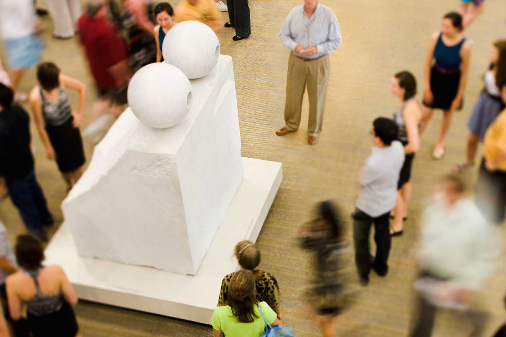 A large white marble sculpture in a room surrounded by people.