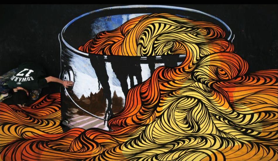 A man painting a large shiny bucket with long colorful pasta flowing out