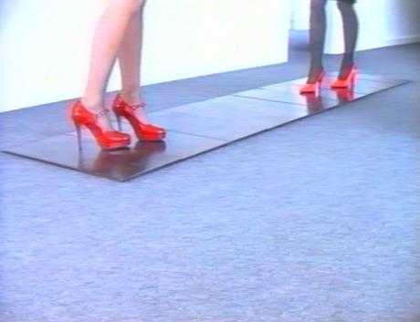 Women's feet in tall red stilleto heels walking on works of art