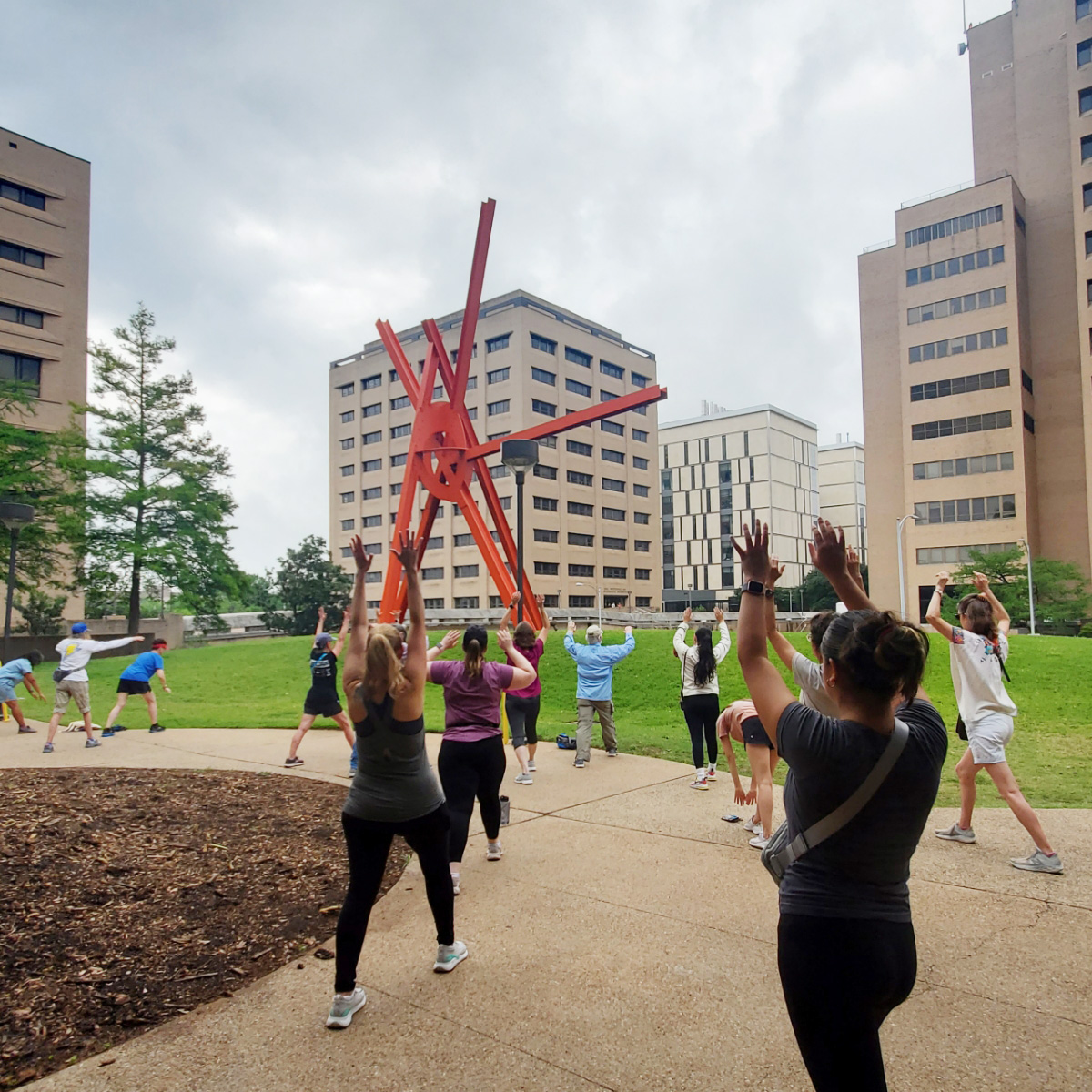 A group of people exercise in front of Mark di Suvero's "Clock Knot"