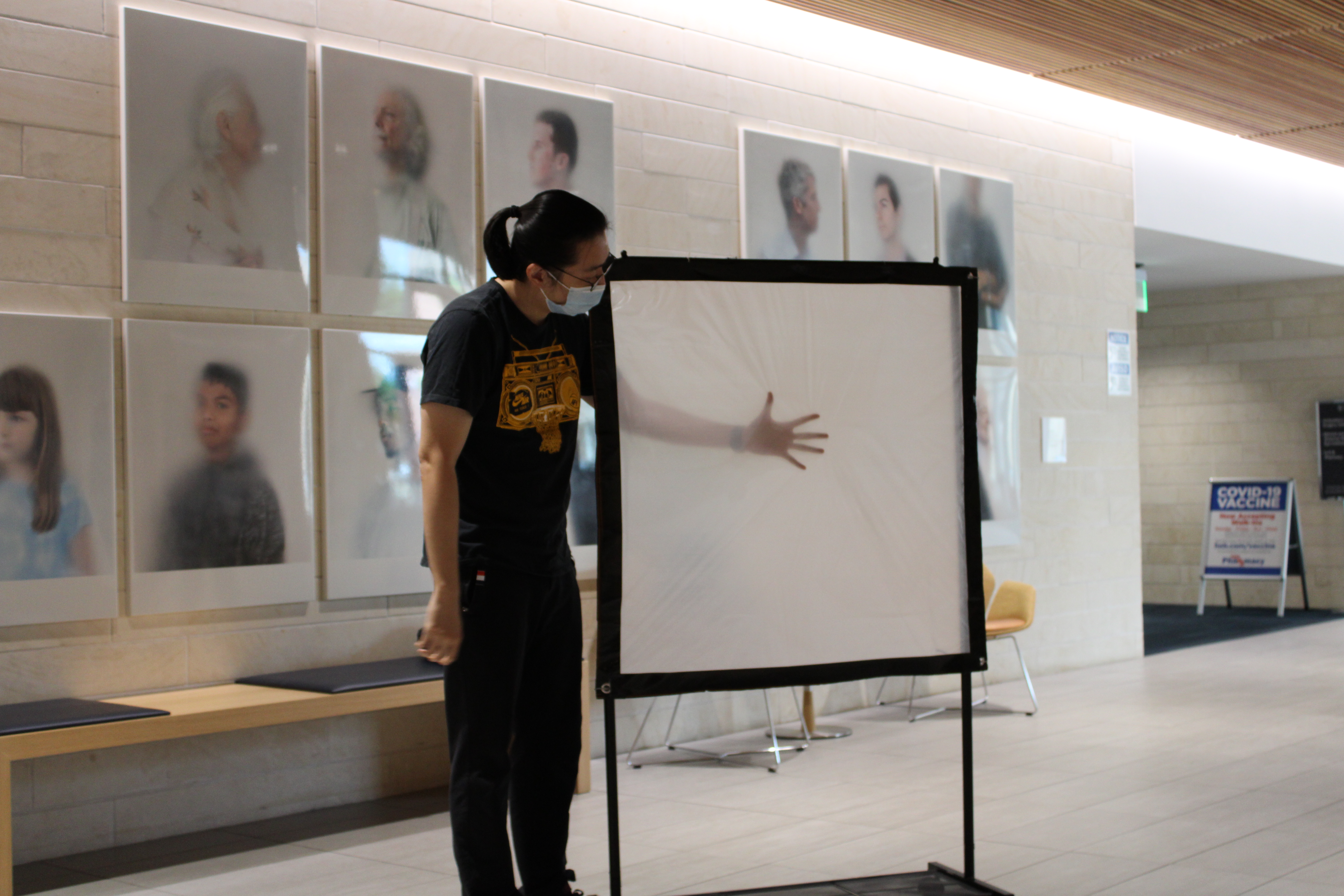 A student holds their hand behind a opaque screen which resembles Ann Hamilton's process in "ONEEVERYONE"