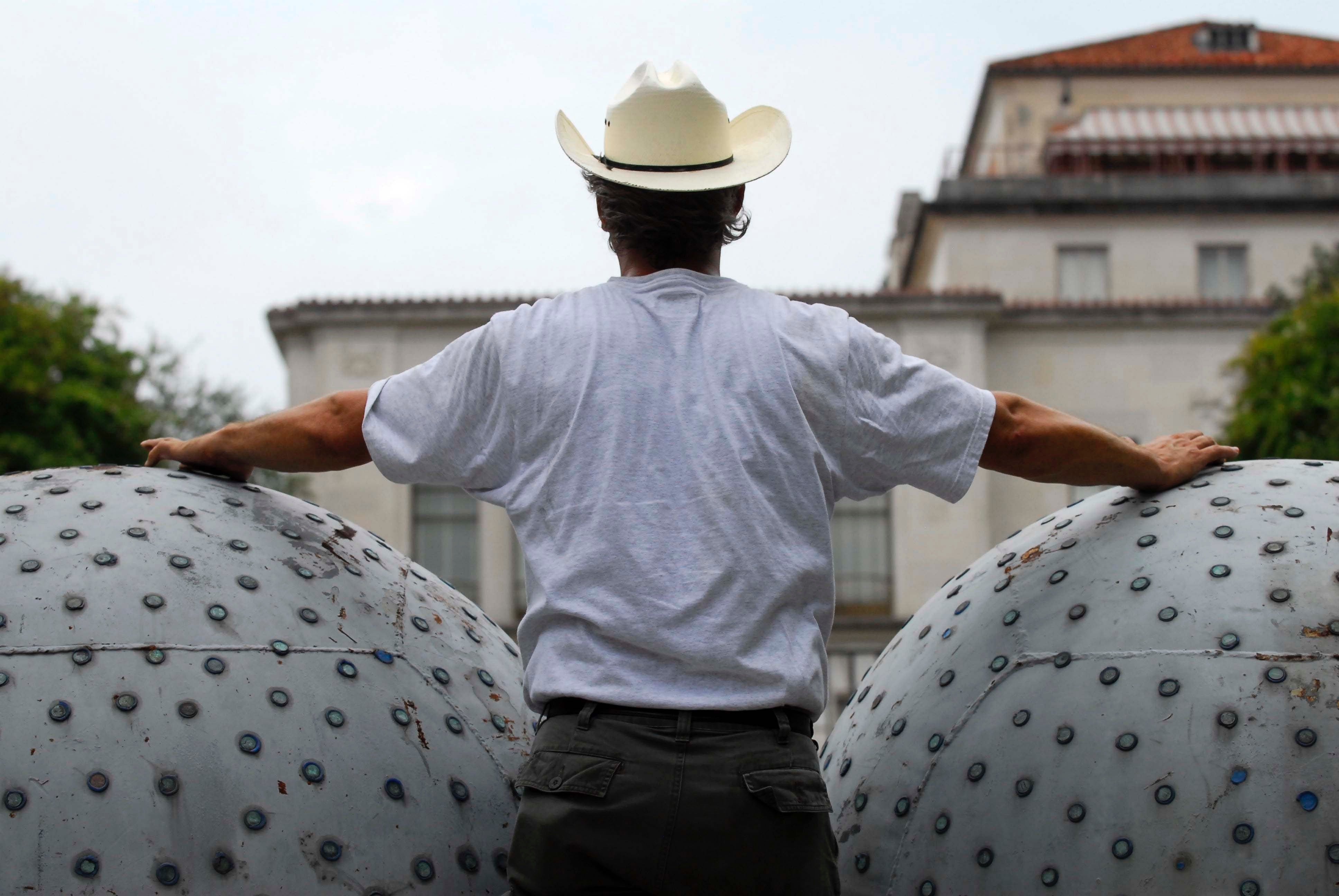 A man wearing a cowboy hat stands between the two large buoys that make up Donald Lipski's The West
