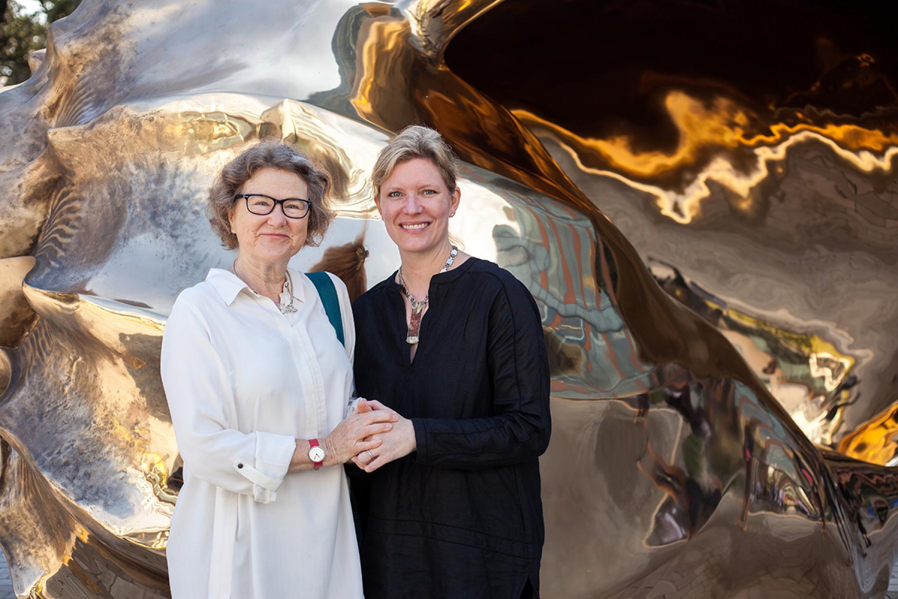 Two women stand in front of large shell (Marc Quinn's, "Spiral of the Galaxy") which appears golden.