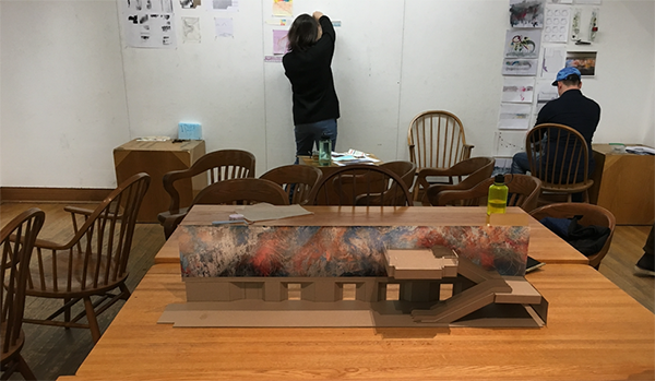 two people working in an architecture studio, with scale model of building on table