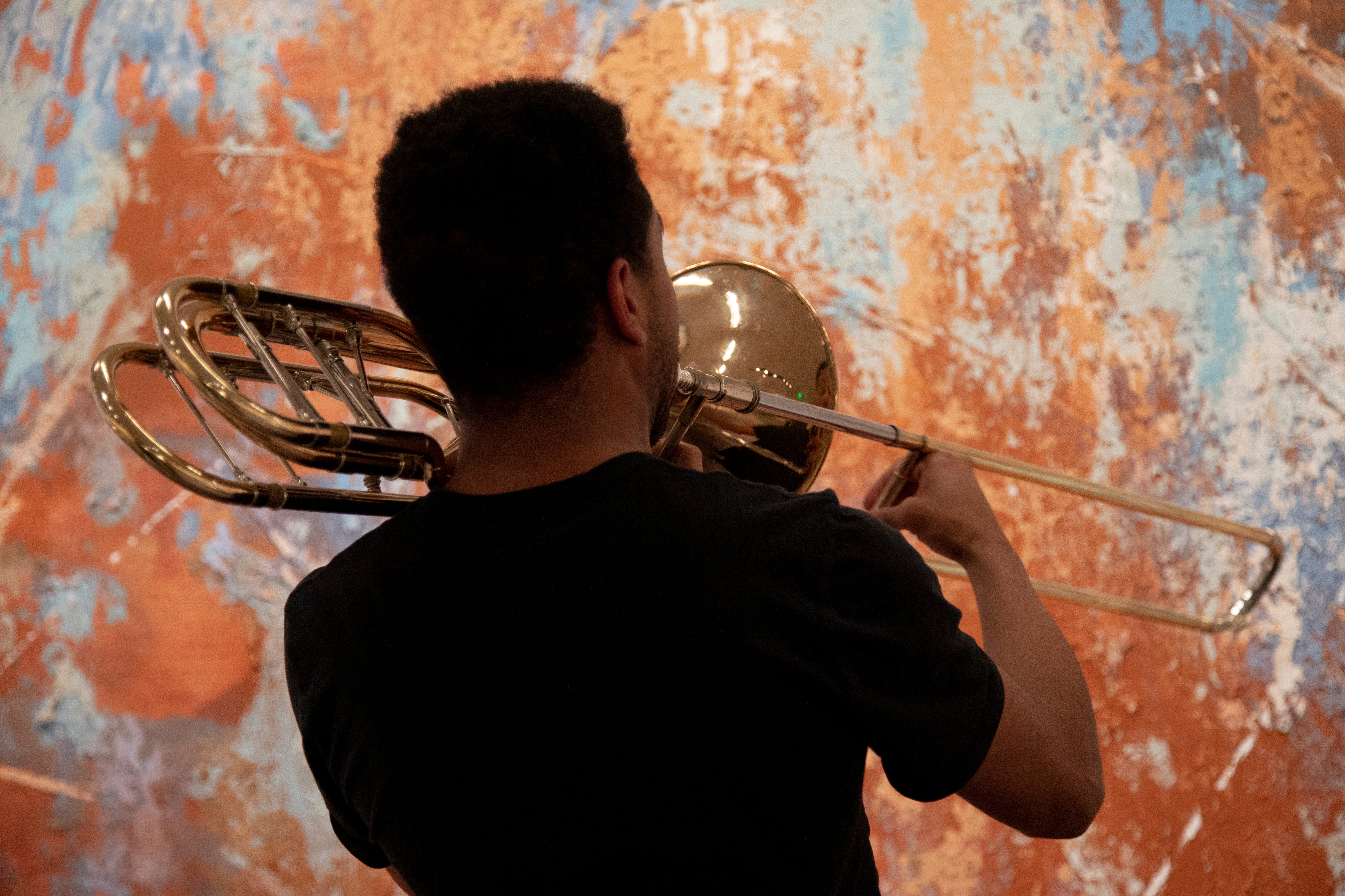 A student plays a trombone towards Jose Parla's mural which can be seen in the background as an array of orange and blue hues 