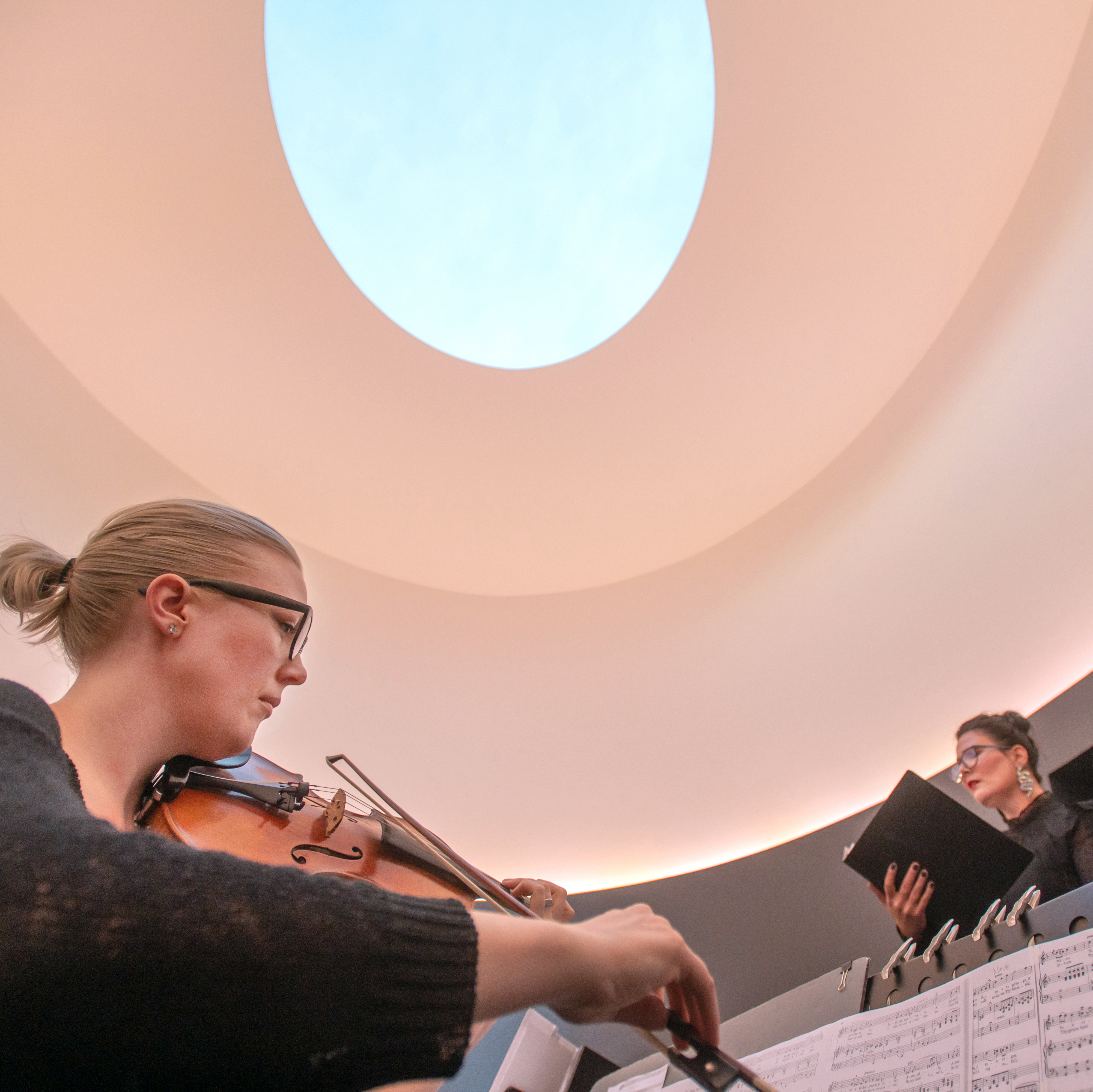Two musicians perform under the oculus of James Turrell's "The Color Inside"
