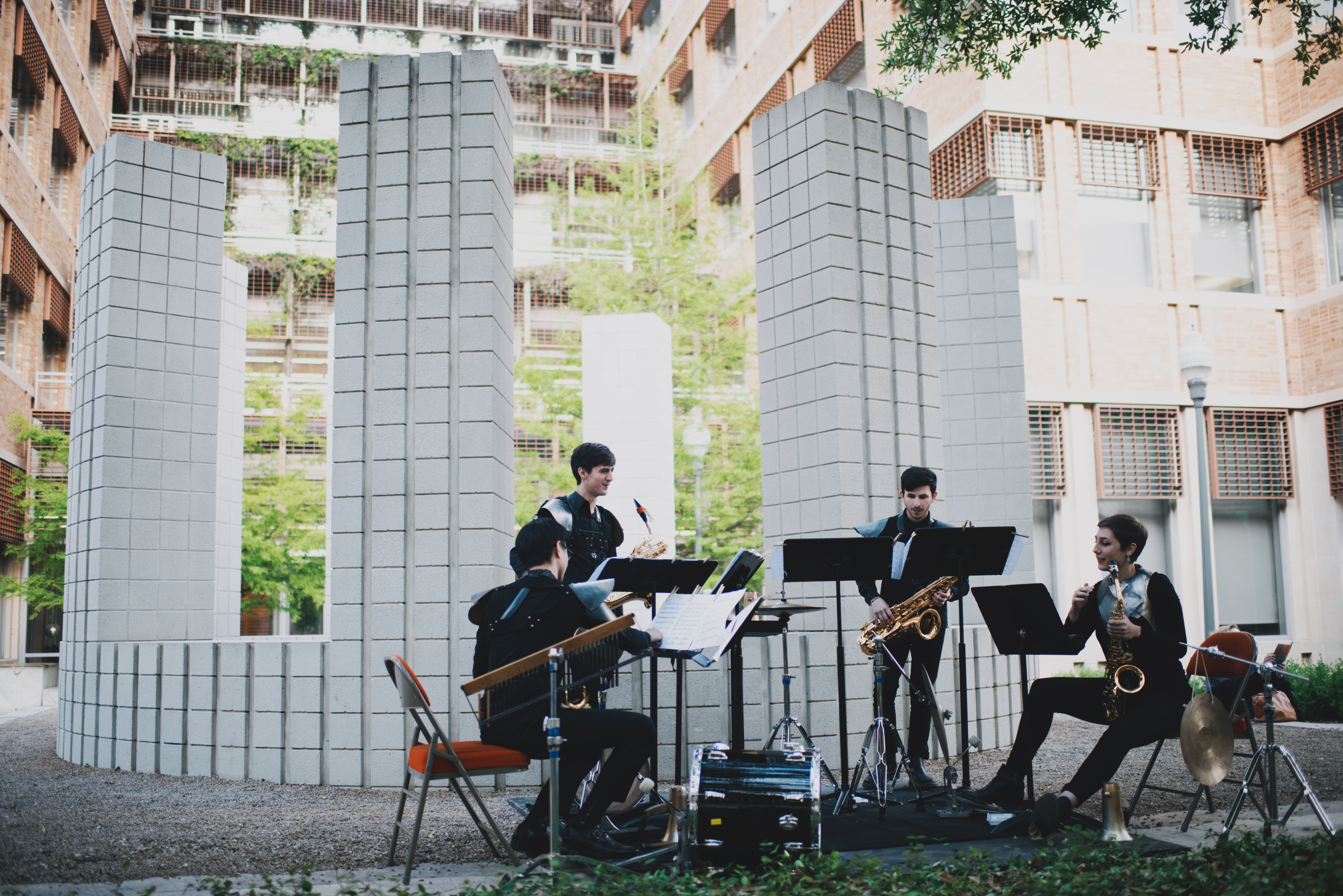 Four performers dressed in black play an assortment of instruments in front of Sol LeWitt's "Circle with Towers" a white concrete structure with tall towers topping a low wall.