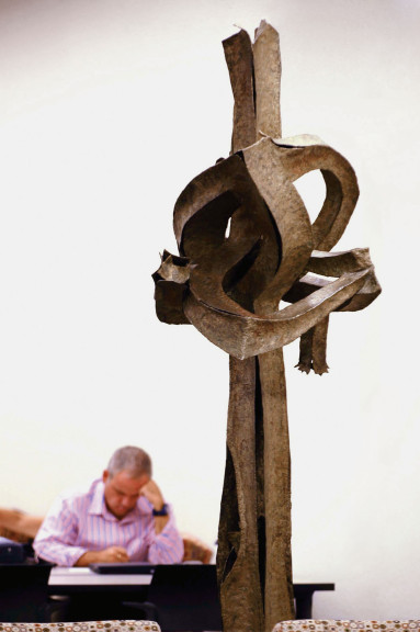A man reading behind a large vertical sculpture