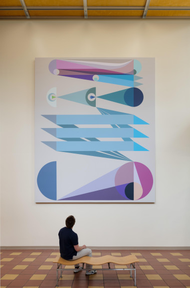 An image of Eamon Ore-Giron's "Tras los ojos," a large digital print which hangs in the atrium of a building. A man sits on a bench in front of the work.