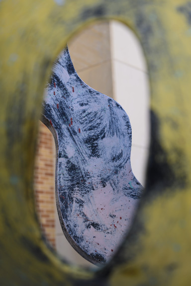 A detail of the sculpture as seen through a cut hole in the sculpture. The area surrounding the hole is back and yellow and the squiggly shape seen through the hole is back and pink