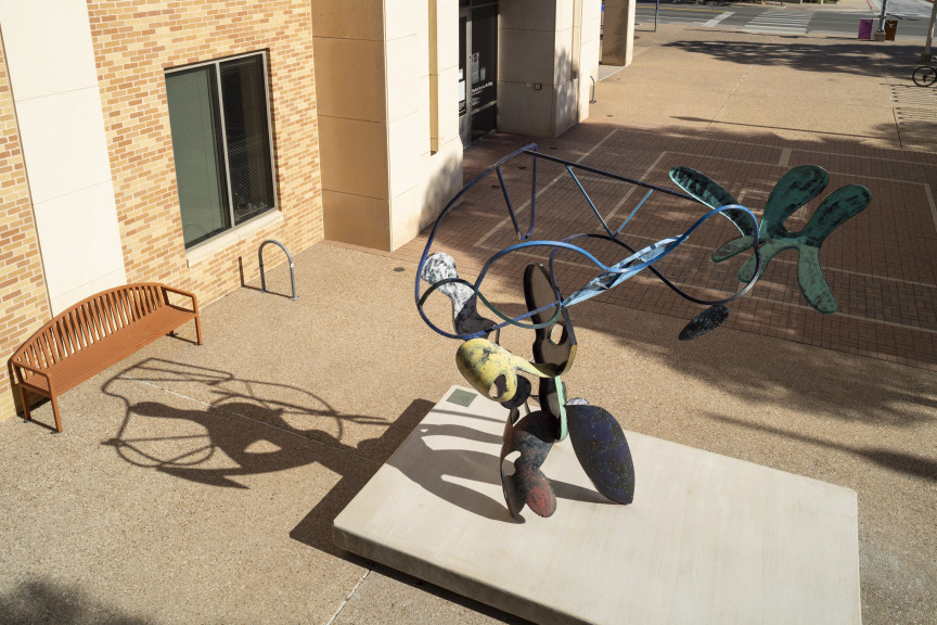 A large bendy sculpture with parts colored in different colors in a courtyard as seen from above