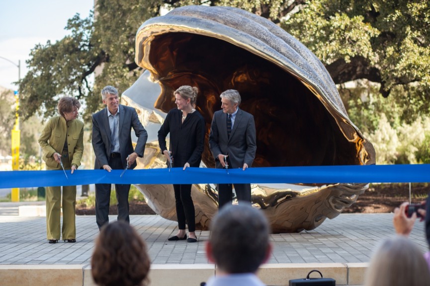 Four people about to cut a large ribbon in front of a bronze shell