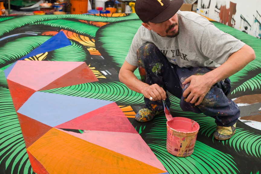 A man squatting over a large art mural on the ground
