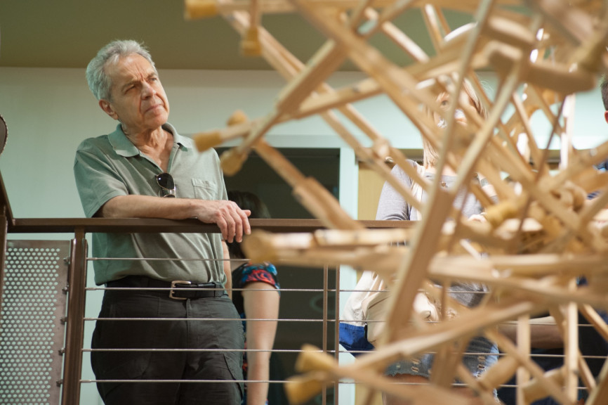 A man looking at a hanging sculpture made out of wooden crutches