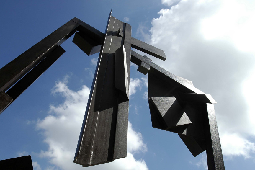 A view looking up at sculpture of steel with blue sky in background