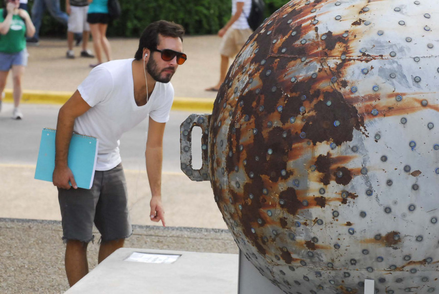 guy with sunglasses on leaning over looking at sphere shaped sculpture