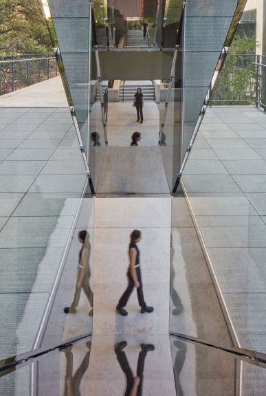 A detail of Sarah Oppenheimer's "C-010106," which shows the reflective quality of the work. Three people are caught in motion through the reflection of the work.
