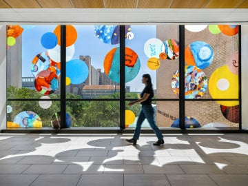 Interior view of "Autobiography: Circles" with a person walking past a brightly lit window with colored circles on the facade