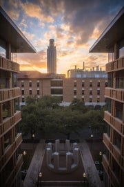A circular symmetrical concrete structure with a tower in the background at sunset