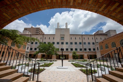 Sentinel IV, seen from behind. The work is centered in a landscaped courtyard. An apeture created by the building frames the work in this image with the circular ceiling coming down and two staircases framing the bottom edge.
