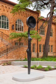 The artwork, Sentinel IV, a tall slender female figure with a bowlcrown for a head is seen from the left.