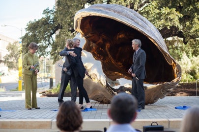 People embracing in front of a bronze shell