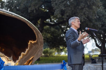 A man talking in front of a ribbon and bronze shell