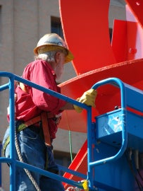 A man working on a large red metal sculpture