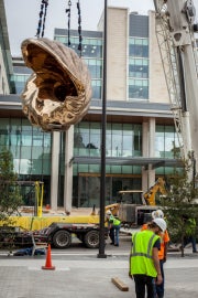 A bronze shell hanging from a crane with a crew member standing in the foreground